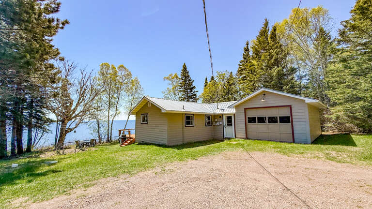 A charming lakefront cottage with convenient parking, surrounded by mature trees and natural landscape in a peaceful wooded setting.