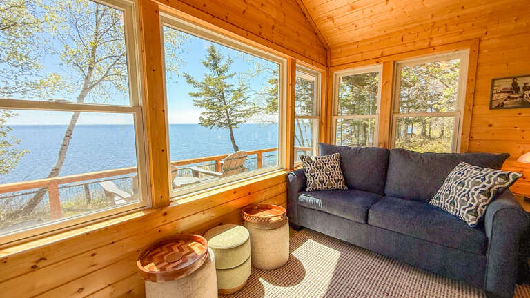 Sink into this cozy sofa and watch the lake shimmer through floor-to-ceiling windows, framed by warm pine walls that make every moment here feel like a peaceful retreat.