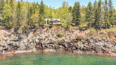 Waterfront property nestled atop rugged cliffs overlooking crystal-clear lake waters, surrounded by towering evergreens and seasonal foliage, offering a secluded and scenic lakeside retreat.