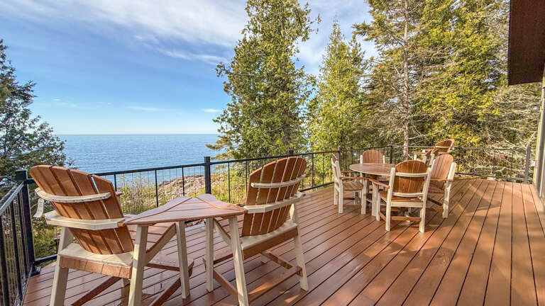 A spacious lakefront deck offers sweeping water views framed by towering pines, with comfortable seating for outdoor relaxation and dining in the fresh air.