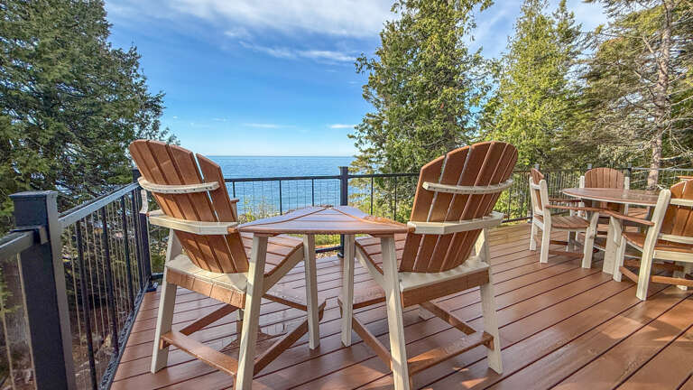 Imagine sipping your morning coffee in these comfortable Adirondack chairs, overlooking stunning blue waters framed by lush trees. This peaceful deck offers the perfect lakeside escape for relaxing moments.