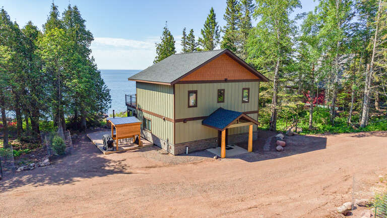 Charming lakefront property nestled among towering pines with expansive lake views, featuring a private covered parking area and a deck overlooking the serene shoreline.