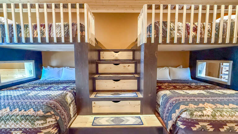Your family's perfect sleeping space awaits with custom-built bunk beds, thoughtful storage stairs, and cozy quilts that welcome everyone to rest together in style.