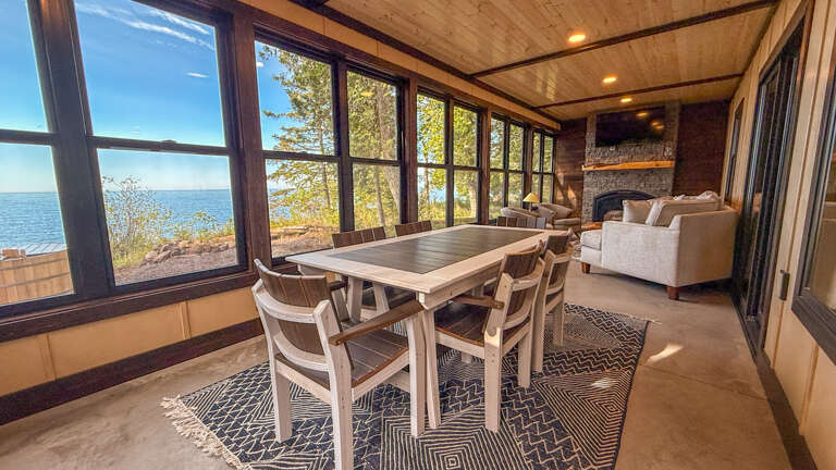 Imagine morning coffee at this lakeside table, where panoramic windows frame shimmering waters and forest views, and a cozy stone fireplace waits to warm your evenings.