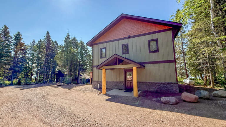Modern mountain retreat with welcoming entrance, nestled among tall pines with generous parking and a covered front porch for arrival convenience.