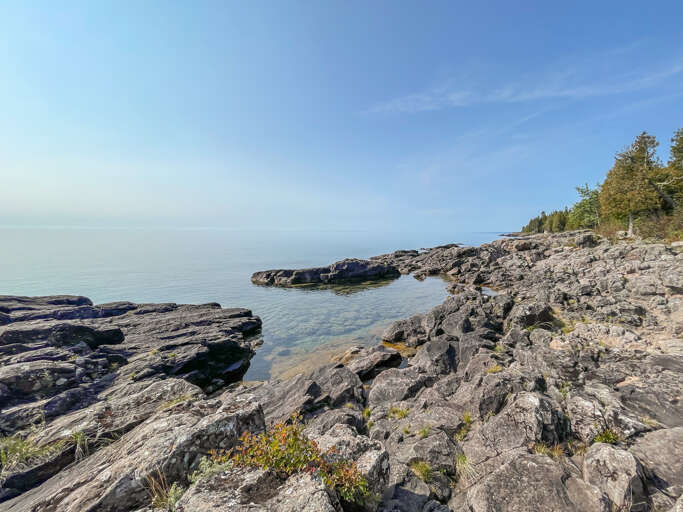 Pristine shoreline with rugged rock formations and calm waters, framed by evergreen trees along this tranquil lakeside retreat.