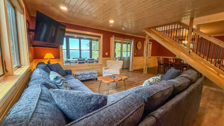 Sink into plush sofas by the warm glow of lamps as you gaze out at stunning lake views. The wood-paneled ceiling and open layout create a cozy, inviting retreat perfect for gathering with loved ones.