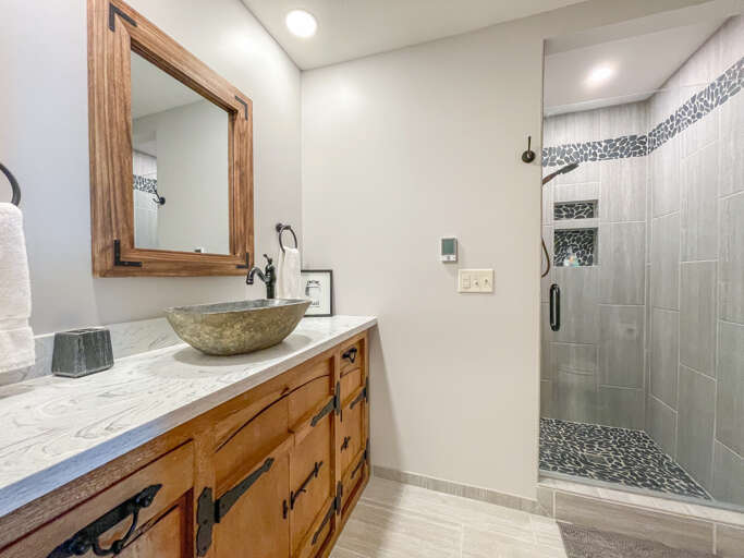 You'll love the natural stone vessel sink and stunning walk-in shower with pebble accents, blending rustic charm and modern spa-like elegance in your private bathroom retreat.