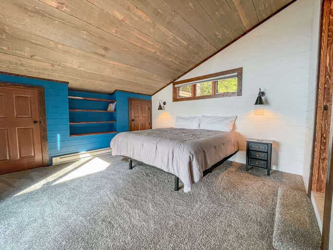 Settle into your cozy loft bedroom, where vaulted wood-plank ceilings and warm reading lights create a peaceful retreat. Wake to sunlight streaming through your window onto soft carpets underfoot.
