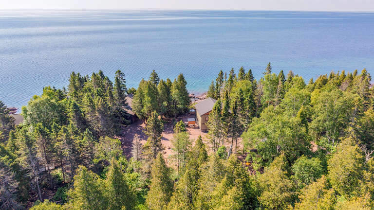 Secluded waterfront property nestled among evergreens and birch with private beach access on tranquil blue waters.