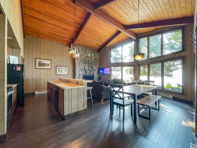 Gather around the dining table where soaring cathedral ceilings and a stunning stone fireplace frame your waterfront views through floor-to-ceiling windows, creating the perfect retreat for memorable meals and cozy evenings.