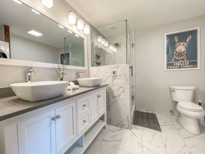 Freshen up in this beautifully appointed bathroom with dual vessel sinks, gleaming marble finishes, and a spacious glass-enclosed shower. Modern fixtures and abundant lighting make your morning routine feel effortless.