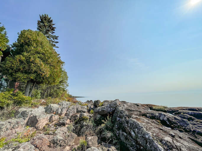 Rugged coastline with rocky shores and towering evergreens frame this peaceful waterfront setting, offering a serene backdrop to the property's natural surroundings.