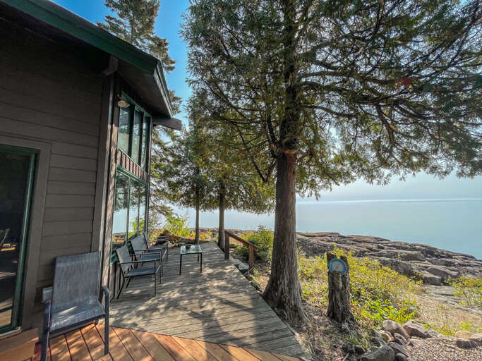 Waterfront retreat with sweeping lake views from your private deck, framed by towering pines and rugged shoreline. Unwind in nature's embrace with seating for two and endless tranquil waters.