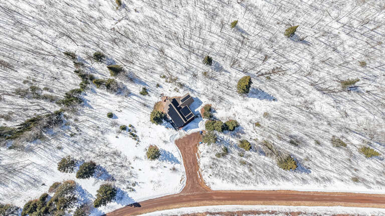 Aerial view of an isolated mountain retreat surrounded by pristine winter wilderness and snow-covered natural landscape.