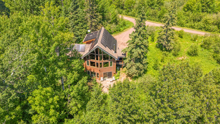 Aerial view reveals a striking cedar-sided retreat nestled privately among lush green forests, with winding driveways providing easy access to this secluded woodland setting.