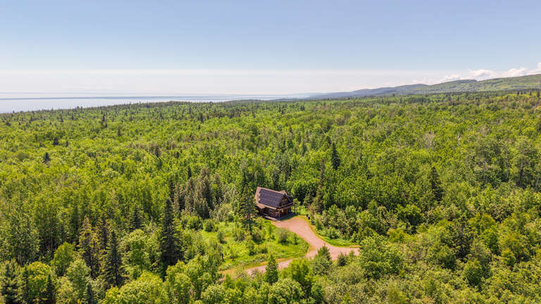 Secluded cabin nestled within vast forest offering complete privacy, with expansive lake and mountain vistas stretching to the horizon.
