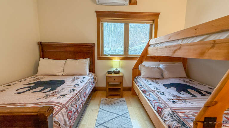 Cozy bedroom with bunk bed and double bed, perfect for families. Enjoy forest views while you rest. Please note that the top bunk is not available and will not have sheets or a blanket.