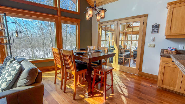 Gather for memorable meals in this warm dining space, where natural light streams through expansive windows and rich wood details create the perfect atmosphere for your getaway conversations.