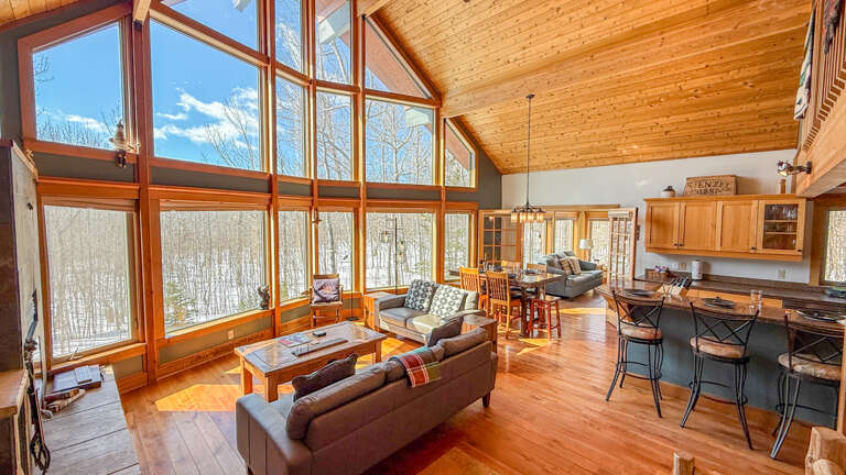 Relax in your open-concept retreat with soaring wood ceilings and floor-to-ceiling windows framing serene winter forest views.