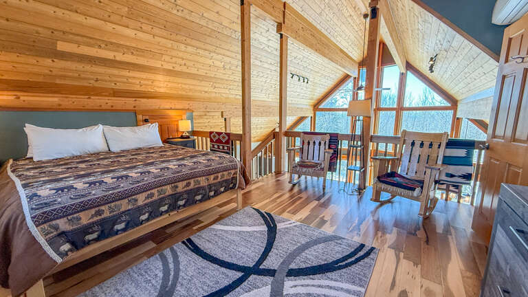Your rustic loft bedroom features soaring wood ceilings, cozy seating, and stunning panoramic windows for peaceful mountain mornings. Open to the Great Room below.