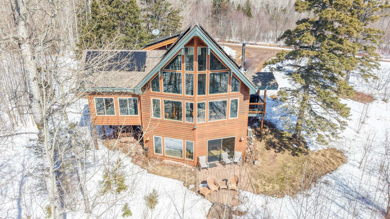 A stunning cedar cabin nestled in winter woods, featuring soaring windows that frame snowy landscapes and evergreen trees.