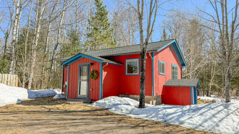 Charming red cabin nestled among snow-dusted trees, offering a cozy winter retreat with rustic charm and peaceful forest surroundings.