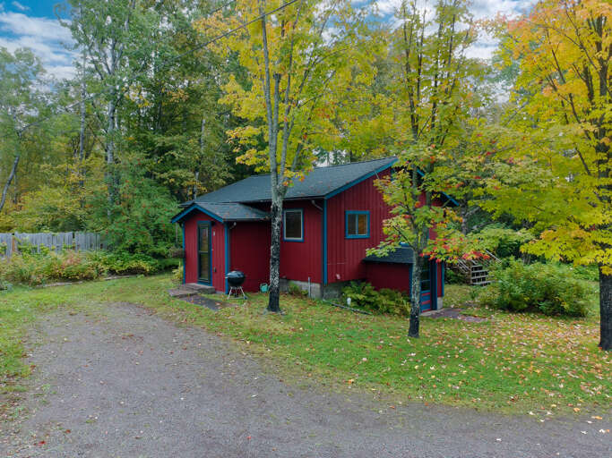 A charming red cabin nestled among vibrant autumn foliage, offering a peaceful retreat surrounded by nature's seasonal beauty.