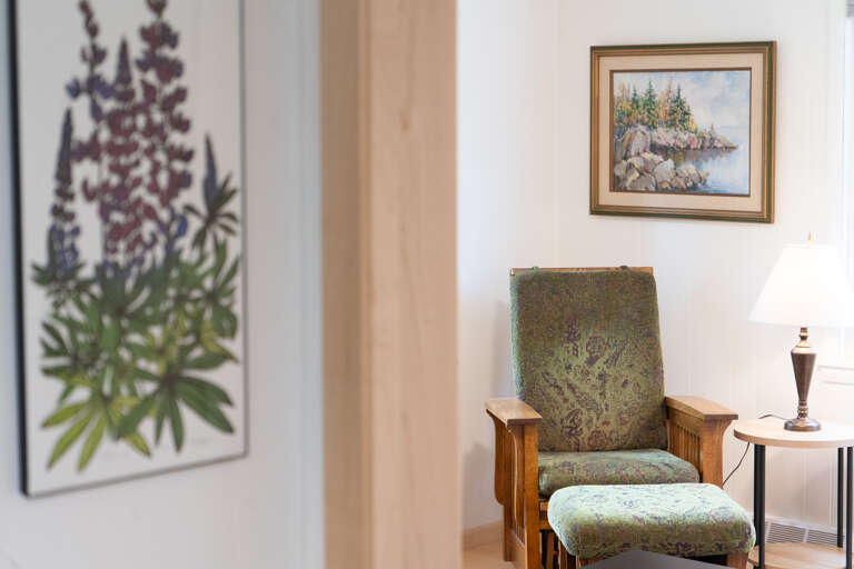 Settle into this inviting reading nook with a vintage armchair and ottoman, where coastal artwork and soft natural light create your perfect spot to unwind with a good book.