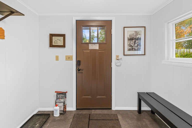 Your welcoming entryway opens onto a bright, clean space where natural light streams in through the door and window. A simple bench waits for you to drop your bags after a day of adventure.