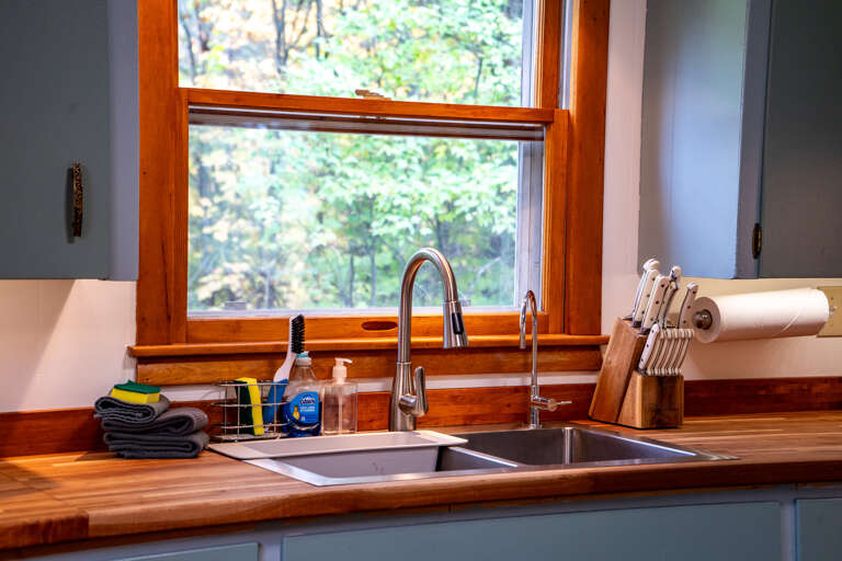 Your fully-equipped kitchen features warm wood countertops and a serene natural view through the window—perfect for brewing morning coffee while looking out at the trees.