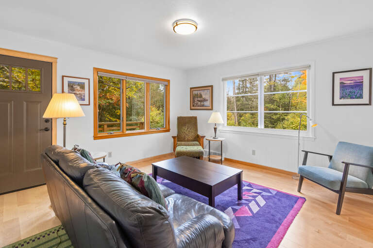 Settle into your bright, welcoming living room where natural light streams through large windows framing leafy views. Your comfortable seating invites you to unwind with a book or simply soak in the serene, forested surroundings.