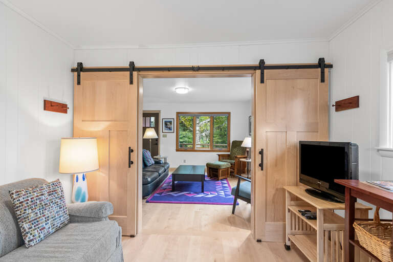 Slide open the handsome barn doors to reveal your spacious living area, where natural light streams through windows overlooking lush greenery and cozy seating invites you to settle in.