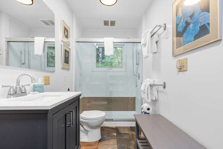 Your private bathroom features a spacious walk-in shower with glass doors, bright natural light, and fluffy white towels ready for you. The clean, modern design creates a peaceful retreat.