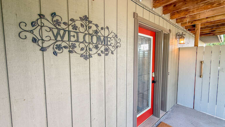 The covered entryway greets you with a charming Welcome sign and a bright red front door, setting a warm and inviting tone for your arrival at the property.
