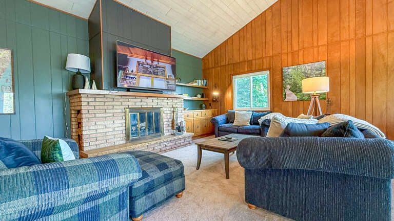 Cozy up in this inviting living room with vaulted ceilings, warm wood paneling, and a charming brick fireplace. Your windows open to peaceful greenery, making it the perfect spot to unwind.