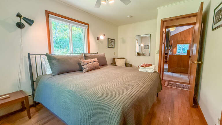 Your serene bedroom awaits, featuring warm hardwood floors, a cozy queen bed dressed in soft linens, and natural light streaming through a peaceful garden window.