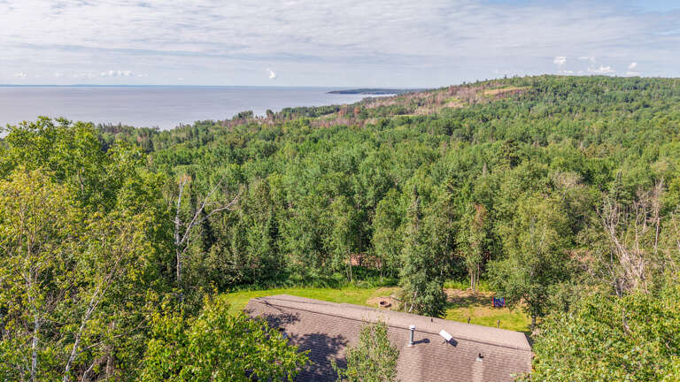 Aerial view of the property nestled among lush forest with breathtaking sea views in the distance—a serene, nature-surrounded retreat.