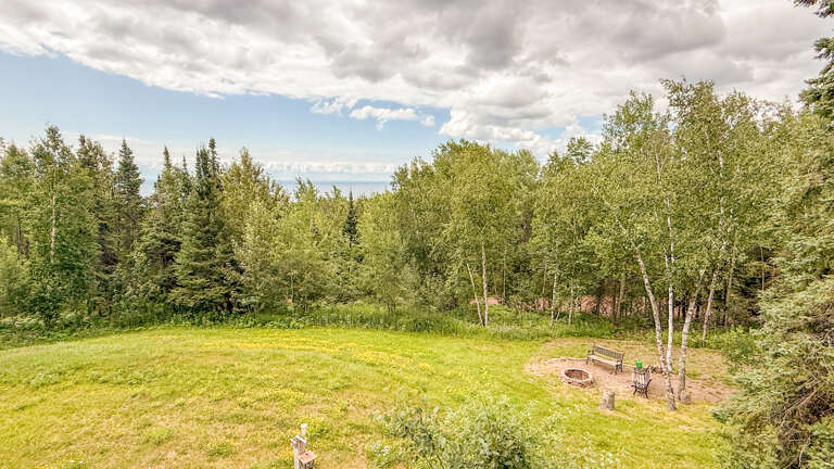 The property sits on a tranquil hillside surrounded by lush forest and expansive open lawn, offering a peaceful natural setting with distant mountain views.
