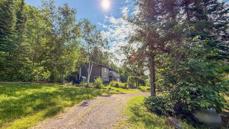 Nestled among lush trees and greenery, this charming property welcomes you with a private gravel driveway and peaceful natural surroundings, perfect for your getaway retreat.