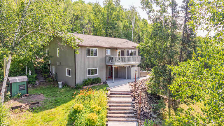 A spacious two-story home nestled in a wooded setting, featuring a private balcony and landscaped grounds surrounded by mature trees.