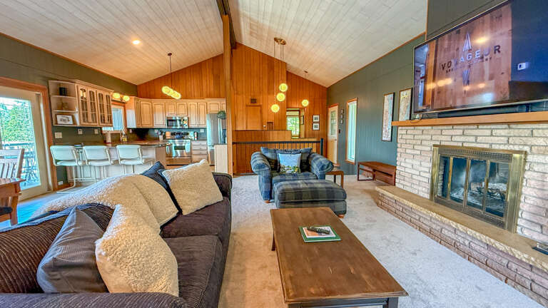 Step into your open-concept retreat with soaring vaulted ceilings, cozy seating by the stone fireplace, and a fully equipped kitchen ready for your meals together.