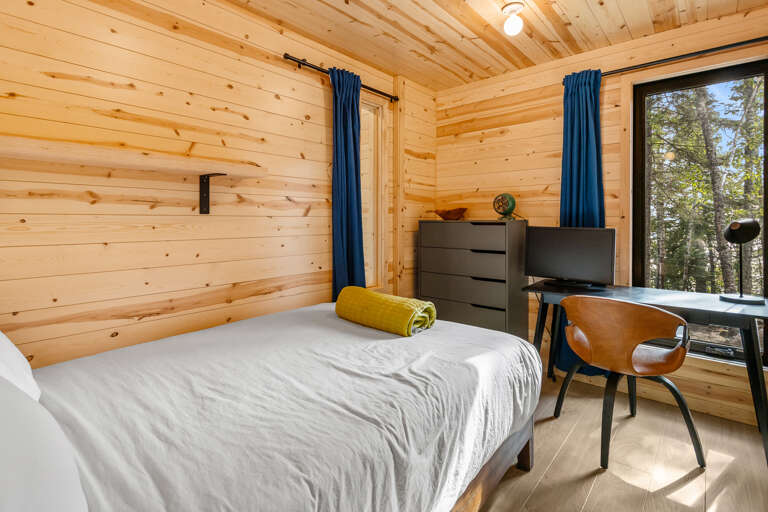 Wake up surrounded by warm pine walls and natural light streaming through your window, overlooking peaceful forest views. Your cozy retreat features modern furnishings and a dedicated workspace—perfect for unwinding after a day of adventure.