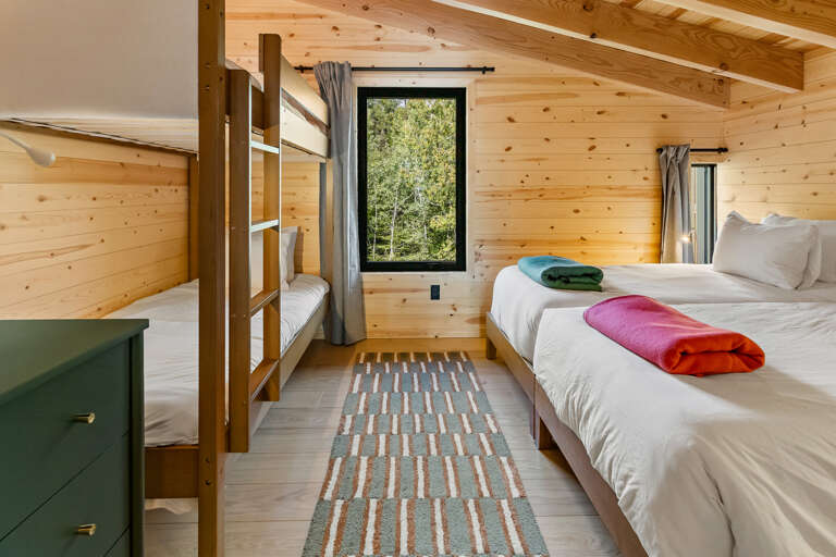 Unwind in this cozy cabin bedroom, where warm pine walls and vaulted ceilings create your mountain retreat. Fresh linens and colorful towels await your arrival.