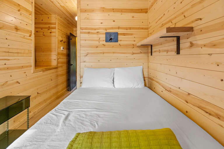 Cozy up in your cabin-style bedroom with warm wood walls and fresh white linens waiting for your arrival.