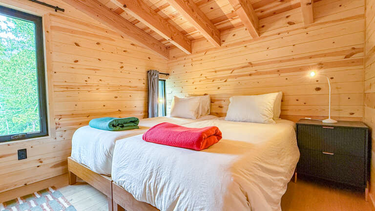 Step into your cozy wooden retreat, where natural pine envelops you in warmth. Fresh towels await on your crisp beds, and sunlight filters through the window, inviting tranquil mornings and restful nights.