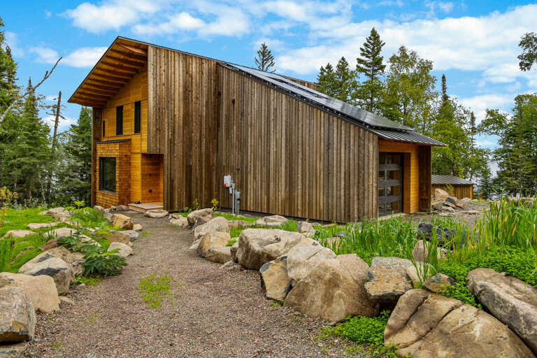 This striking modern retreat features natural wood architecture set among rocks and lush greenery, offering a peaceful arrival to your woodland escape.