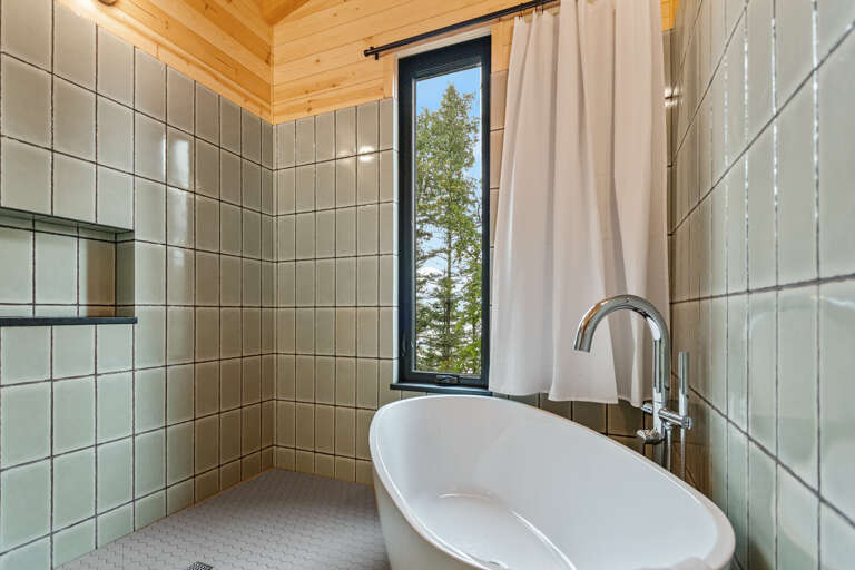 Slip into your freestanding soaking tub and soak up the peaceful view through the window. Natural light brightens the sleek tile and warm wood finishes, creating a spa-like retreat for unwinding after your adventures.