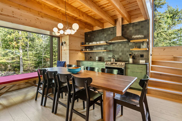 Gather around the handcrafted wood table in this sun-drenched dining space, where exposed beams meet modern style and forest views frame every meal.