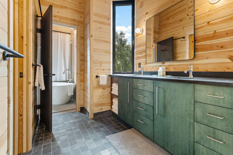 Refresh in your private bathroom featuring warm wood walls, a sleek double vanity, and fluffy towels waiting for you. Step through to discover a soaking tub framed by natural light.